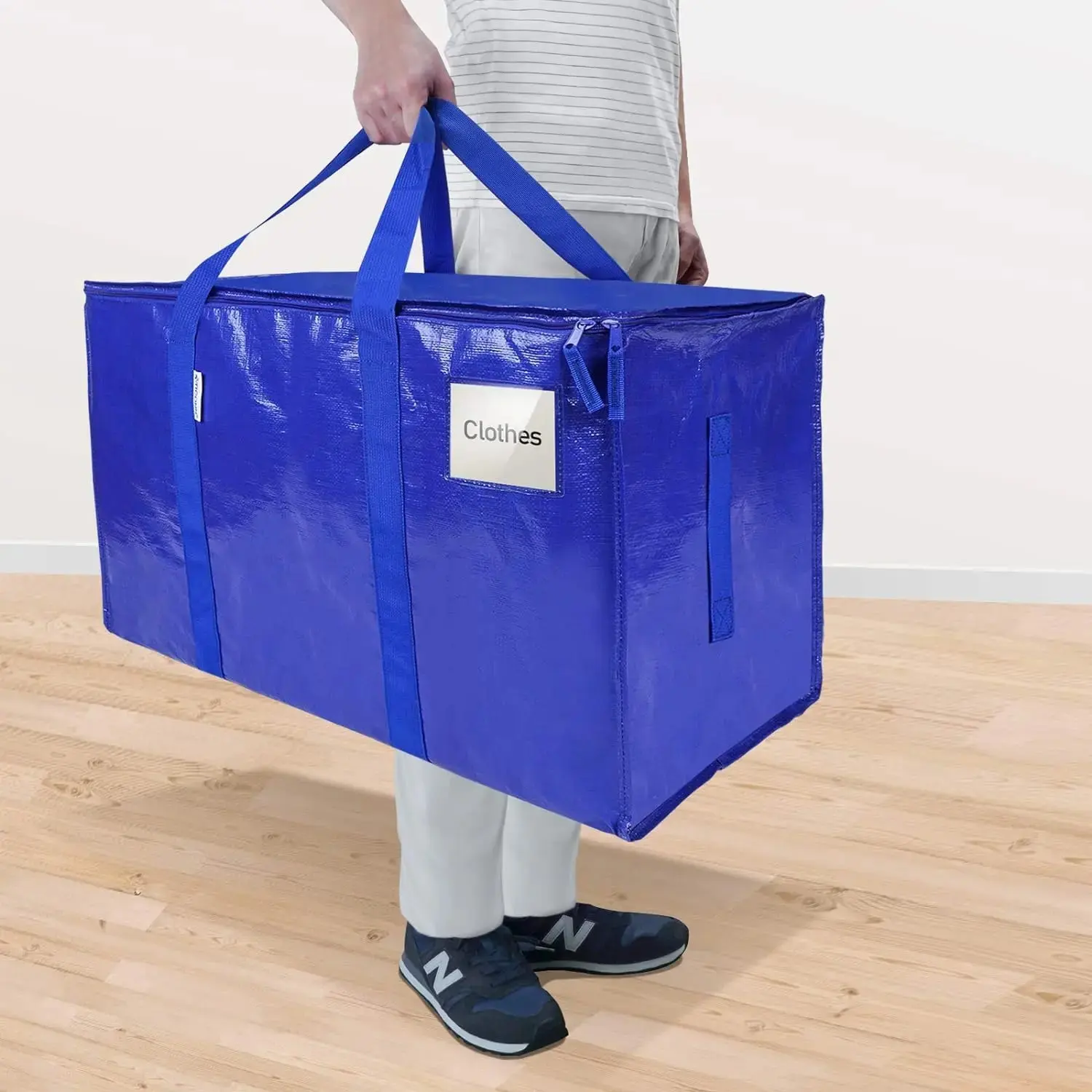 Person carrying a cobalt blue CasaBella moving bag by the wrap-around handles, with a phone in the front pocket